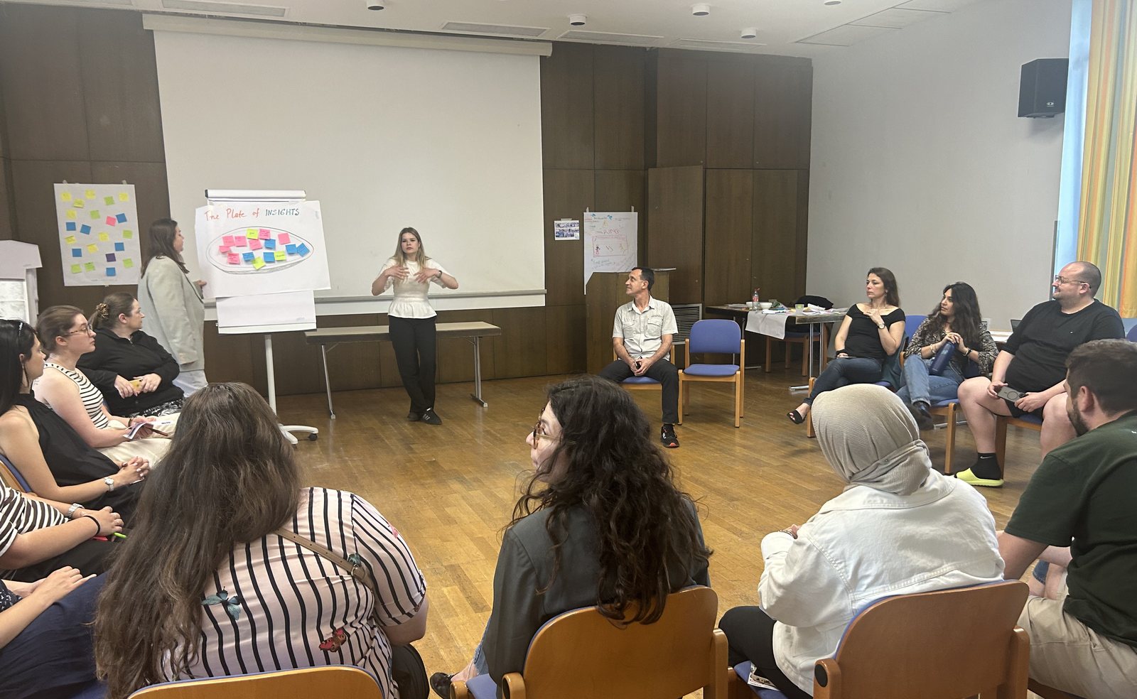 Participants seated in a circle during the SDGs Intelligence Cards training, with a facilitator and flipcharts of sticky notes